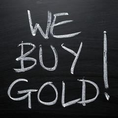 The phrase We Buy Gold written by hand in white chalk on a blackboard