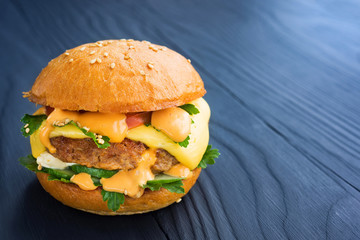 Tasty homemade burger with tomato, cucumber, parsley, sauce and cheese, on a wooden dark background.