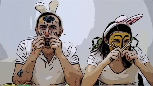 Cute and adorable couple came back to childhood. Man is holding two paint-brushes in his hands and a woman is holding four paint-brushes in her. Couple wearing bunny ears. They are making funny