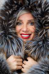 Portrait of middle-aged woman in fashionable jacket with fur isolated on gray background