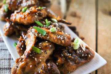Close-up of crispy baked chicken wings, glazed with honey sauce with fresh scallions on wooden background
