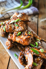 Close-up of crispy baked chicken wings, glazed with honey sauce with fresh scallions on wooden background