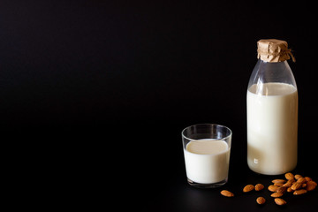 A bottle and a glass of milk next to the almond. Black background.