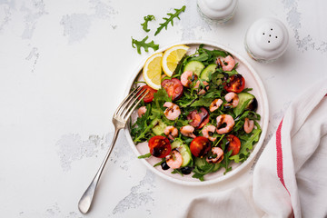 Arugula, cucumber, tomato and shrimp salad with soy sauce on a ceramic plate. Selective focus. Top view.