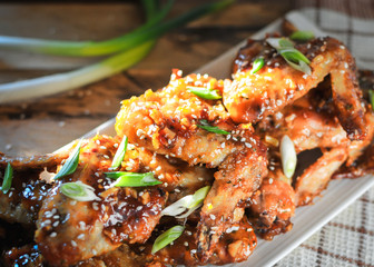 Close-up of crispy baked chicken wings, glazed with honey sauce with fresh scallions on wooden background