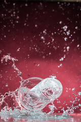 falling one-time transparent glass with clear water and spill water on a red background
