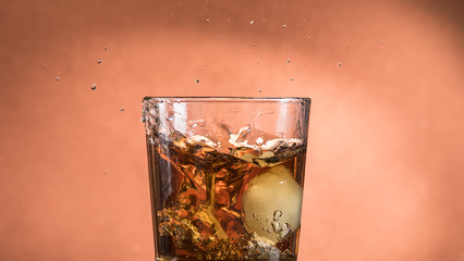 splash in a glass of whiskey with ice on an orange brown background