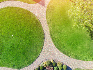 Aerial drone view of backyard garden with circle wath path, green grass lawn and trees. Landscape design and gardening - Powered by Adobe