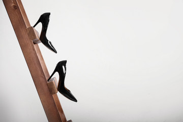 Female shoes on wooden ladder against light background. Concept of career failure