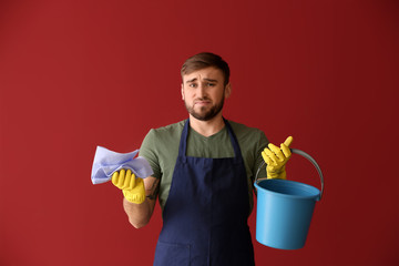 Disappointment lazy man with cleaning supplies on color background