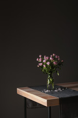 Vase with beautiful roses on table against dark background