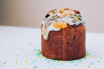 Selective focus Delicious freshly baked Easter cake with icing, nuts, seeds, candied fruit, multicolored sweet sprinkles against white backdrop. Easter, birthday greeting card or web banner concept