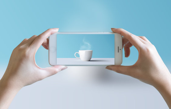 hands take photo of cup of coffee and aroma smoke with mobile smartphone