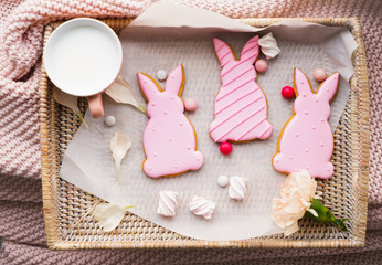 Wicker tray with tasty Easter cookies, candies and milk on bed