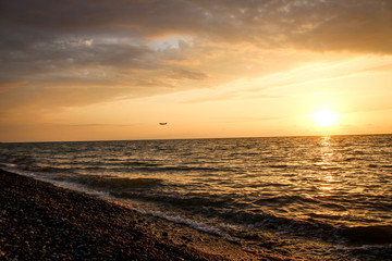 Fototapeta na wymiar Golden, Fiery sunset on the Black Sea, on the beach. Coast, stones, waves, sun, beautiful sky, clouds. August, Batumi, Georgia. Water, ease, game. plane in the sky, tourism