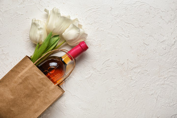 Bag with bottle of wine and flowers on white background