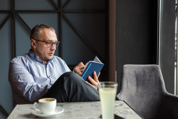 Caucasian middle-aged businessman writing down something in agenda while sitting in cafe