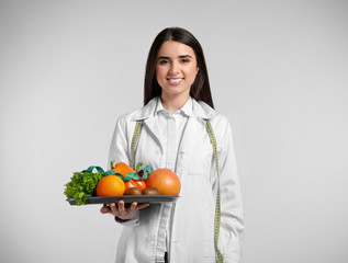 Portrait of female nutritionist with healthy products on light background