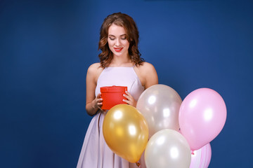 Fototapeta na wymiar Beautiful young woman with balloons and gift on color background