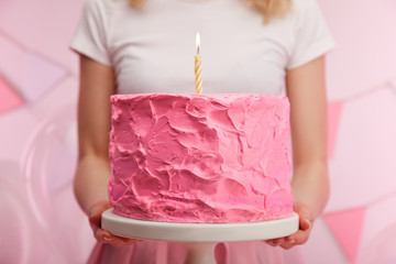 close up of woman holding cake stand with sweet pink birthday cake and burning candle