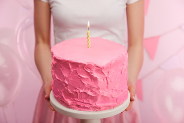 cropped view of woman holding cake stand with tasty pink birthday cake and burning candle