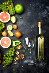 Wine concept. Bottle and glass of young white bio wine with green grapes, grapefruit and other fruit on a gray stone background