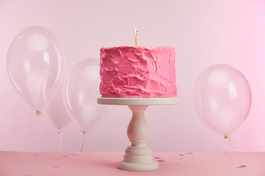 Sweet And Tasty Birthday Cake With Burning Candle On Cake Stand Near Air Balloons On Pink