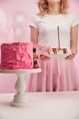 selective focus of delicious birthday cake on cake stand near woman on pink