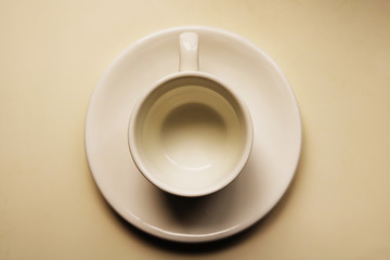 Empty white teacup and saucer on a white table surface - top view, old retro look