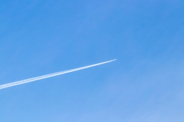 White airplane in blue clear sky leaving white diagonal trace