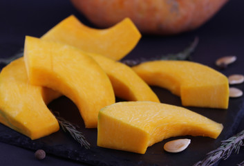 Close-up on a slice of pumpkin, which lies on a dark dish. Blur effect. Ingredients for cooking homemade and wholesome food. Healthy eating concept