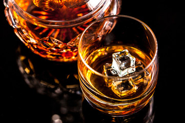 Whiskey glass hold by man hand and crystal decanter on dark background. Selective focus. Copy space.
