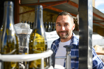 young man wine maker working filling wine bottle with automatic bottling machine