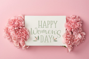 top view of greeting card with happy womens day lettering and pink carnations on pink background