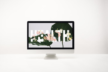 computer with health lettering and tropical green leaves on monitor on desk on white background