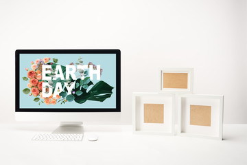computer with earth day lettering on monitor and empty photo frames on desk on white background