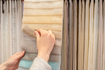 Young woman choosing fabric for new curtains in shop