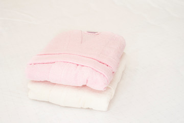 Folded bathrobe on bed in room. White and pink, two robes