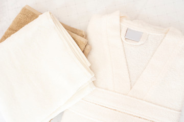 Folded white bathrobe and towels on bed in room