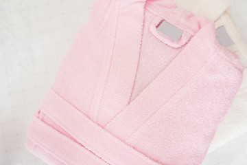 Folded bathrobe on bed in room. White and pink, two robes