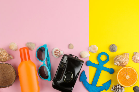 summer accessories with sun glasses, a hat, shells, flip flops, a camera on a bright yellow and pink background. top view. space for text