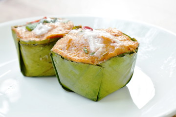 steamed fish with curry paste in banana leaf tray on plate