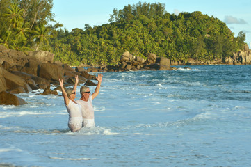 Portrait of happy elderly couple resting on beach waving hands