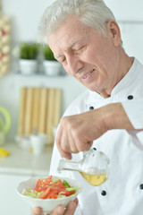Close-up portrait of elderly male chef pouring oil into salad