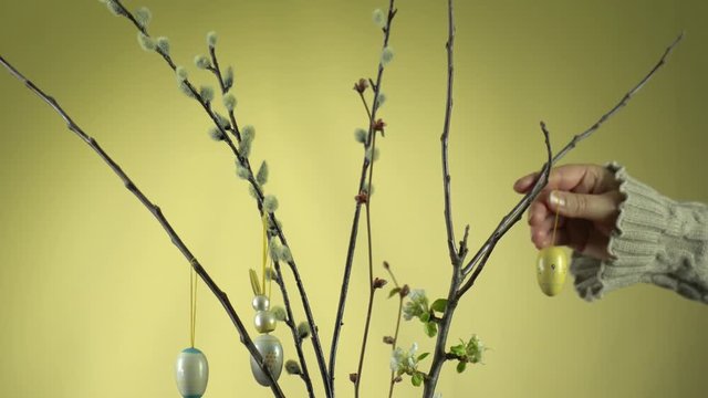 Weidenk&auml;tzchen &Auml;ste und Apfelbaum &Auml;ste in einer Glasvase. Die Apfelbl&uuml;te hat begonnen. Die &Auml;ste werden von einer Frauenhand mit Osterhasen und Ostereiern dekoriert.