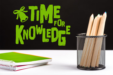 notebooks and color pencils on table with green time for knowledge lettering and bell sign on black