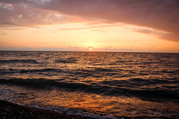Golden, Fiery sunset on the Black Sea, on the beach. Coast, stones, waves, sun, beautiful sky, clouds. August, Batumi, Georgia. Water, lightness, play. Pink, lilac, crimson