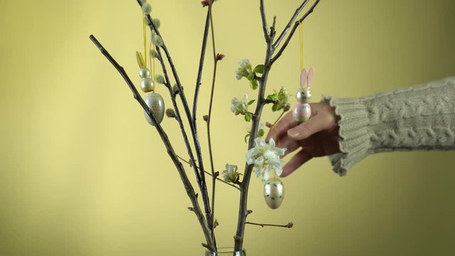 Weidenk&auml;tzchen &Auml;ste und Apfelbaum &Auml;ste in einer Glasvase. Die Apfelbl&uuml;te hat begonnen. Die &Auml;ste werden von einer Frauenhand mit Osterhasen und Ostereiern dekoriert.