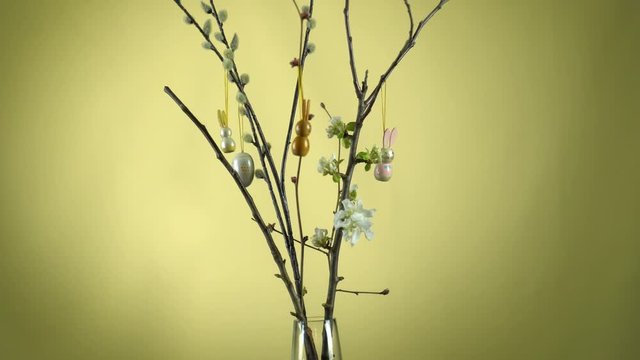 Weidenk&auml;tzchen &Auml;ste und Apfelbaum &Auml;ste in einer Glasvase. Die Apfelbl&uuml;te hat begonnen. Die &Auml;ste werden von einer Frauenhand mit Osterhasen und Ostereiern dekoriert.