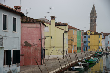 Fototapeta na wymiar Colorful houses in Burano island near Venice, Italy on water canal with boats. In the background the bell tower of the island of Burano.